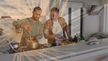 Animation of pasta over diverse male couple cooking dinner in kitchen. Food, drink and lifestyle concept concept digitally generated video.