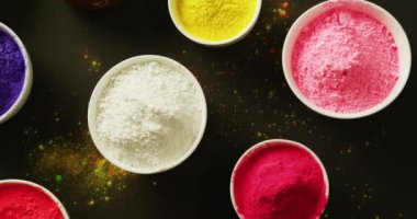 Video of multi coloured powder in bowls with copy space on black background. Holi festival, hindu tradition and celebration concept