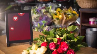 Animation of tablet with heart icons on screen and flowers over florist's. Global business, technology and digital interface concept digitally generated video.
