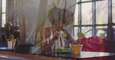 Animation of grass and flowers over african american woman eating salad. Food, drink and lifestyle concept concept digitally generated video.