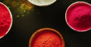 Video of multi coloured powder in bowls with copy space on black background. Holi festival, hindu tradition and celebration concept