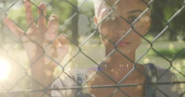 Animation of light trails over biracial woman standing behind fence. Lifestyle, abstract background and digital interface concept concept digitally generated video.