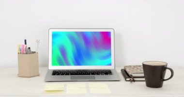 Animation of laptop with colorful moving shapes on screen on desk. Global technology, abstract background and digital interface concept digitally generated video.
