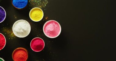 Video of multi coloured powder in bowls with copy space on black background. Holi festival, hindu tradition and celebration concept
