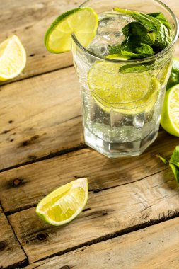 Close up of glass with water and limes with copy space over wooden surface. Cocktail day and celebration concept.