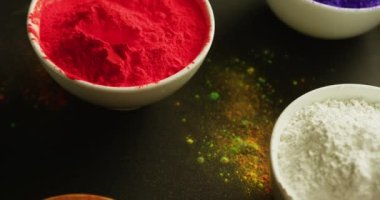 Video of multi coloured powder in bowls with copy space on black background. Holi festival, hindu tradition and celebration concept 