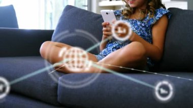 Animation of network of digital icons over caucasian girl using smartphone on the couch at home. Technology and internet concept