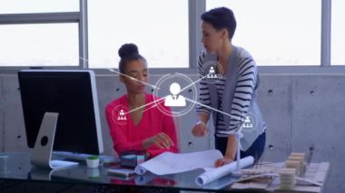 Animation of network of digital icons over two diverse women discussing over a plan at office. Global networking and business technology concept