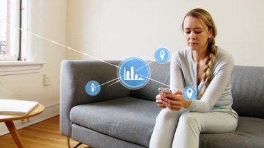 Animation of network of digital icons over caucasian woman using smartphone sitting on couch at home. Global networking and business technology concept