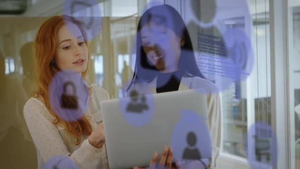 オフィスでラップトップ上で議論する2人の多様な女性の上に複数のデジタルアイコンのアニメーション コンピュータ インターフェースとビジネス技術の概念 — ストック動画