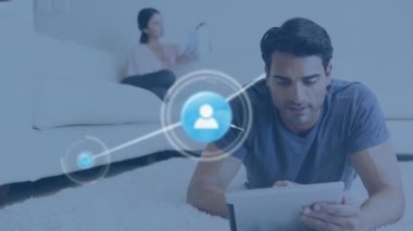 Animation of network of digital icons and light spot over caucasian man using digital tablet at home. Global networking and business technology concept