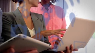 Animation of multiple digital icons over diverse colleagues discussing over laptop at office. Computer interface and business technology concept