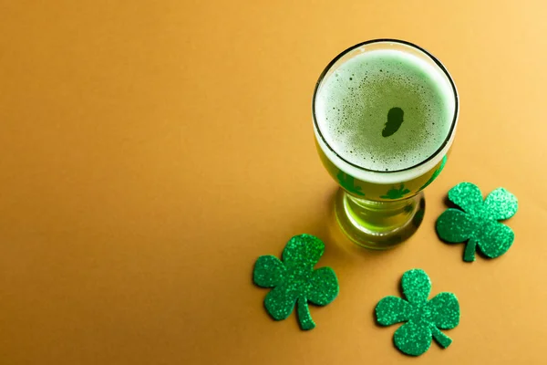 Image of glass with green beer, clover and copy space on orange background. St patrick's day, irish tradition and celebration concept.