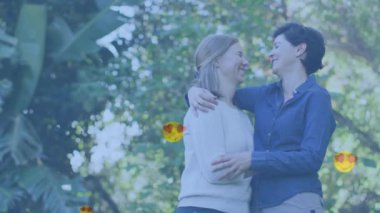 Animation of heart emojis over happy caucasian female couple in love embracing. Love, romance and celebration concept digitally generated video.
