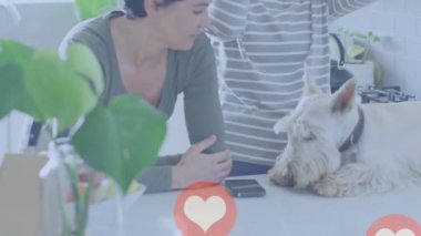 Animation of heart emojis over happy caucasian female couple in love with dog. Love, romance and celebration concept digitally generated video.