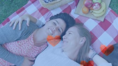 Animation of heart emojis over happy caucasian female couple in love embracing. Love, romance and celebration concept digitally generated video.