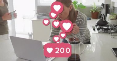 Animation of heart emojis and numbers over happy caucasian female couple in love in kitchen. Love, romance and celebration concept digitally generated video.