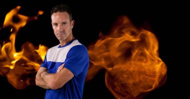 Composition of male basketball player with arms crossed over flames on black background. sport and competition concept digitally generated image.