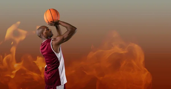 Composition of male basketball player shooting ball, over flames on grey background. sport and competition concept digitally generated image.