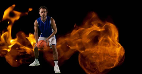 Composition of male basketball player crouching with ball over flames on black background. sport and competition concept digitally generated image.
