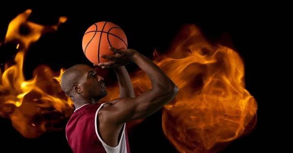Composition of male basketball player shooting with ball over flames on black background. sport and competition concept digitally generated image.