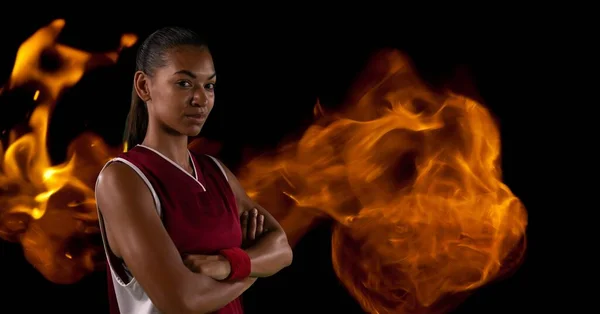 Composition of female basketball player with arms crossed over flames on black background. sport and competition concept digitally generated image.