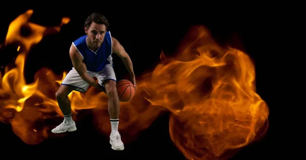 Composition of male basketball player crouching with ball over flames on black background. sport and competition concept digitally generated image.