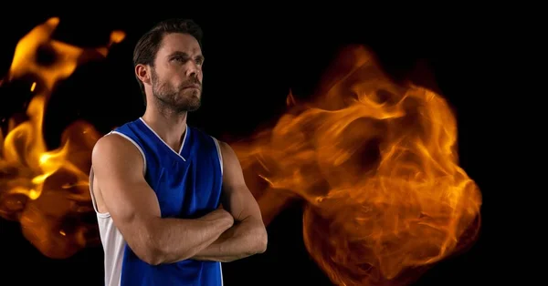 Composition of male basketball player with arms crossed over flames on black background. sport and competition concept digitally generated image.