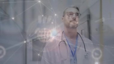 Animation of network of connections with icons over caucasian male doctor at hospital. Global medicine, connections and digital interface concept digitally generated video.