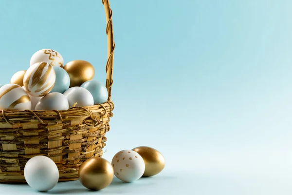 Image of multi coloured easter eggs in basket and copy space on blue background. Easter, religion, tradition and celebration concept.
