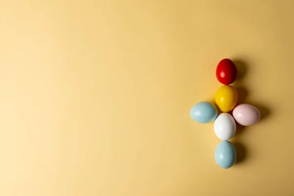 Image of multi coloured easter eggs forming cross with copy space on yellow background. Easter, religion, tradition and celebration concept.