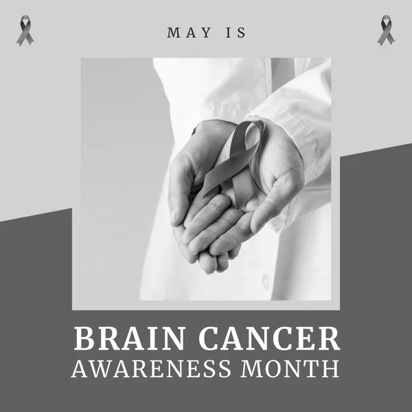 Composition of brain cancer awareness month text over doctor holding ribbon on grey background. Brain cancer awareness month concept digitally generated image.
