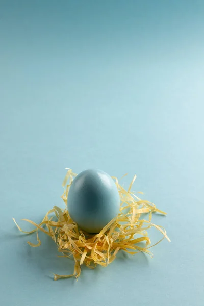 Image of blue easter egg in straw and copy space on blue background. Easter, religion, tradition and celebration concept.