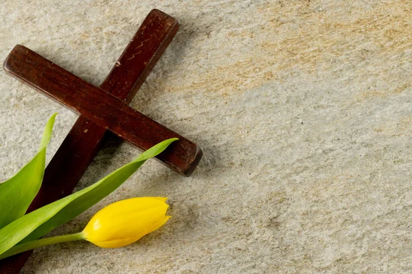 Image of close up of cross with tulip and copy space on stone background. Easter, religion, tradition and celebration concept.