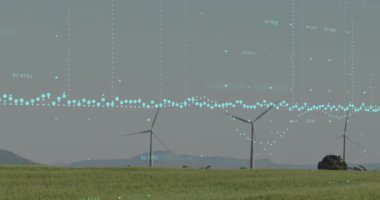 Gri gökyüzüne karşı çayırlarda dönen yel değirmenlerinin üzerinde işlenen verilerin animasyonu. İş verileri ve yenilenebilir enerji teknolojisi kavramı
