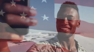 Sahilde akıllı telefon kullanan gülümseyen Afro-Amerikan bir adam üzerinde ABD bayrağının canlandırılması. Amerikan vatanseverliği ve çeşitlilik kavramı dijital olarak oluşturulmuş video.