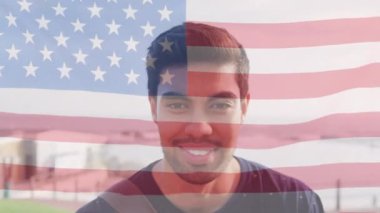 Sahilde gülümseyen melez bir adamın üzerinde ABD bayrağının canlandırılması. Amerikan vatanseverliği ve çeşitlilik kavramı dijital olarak oluşturulmuş video.