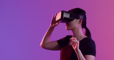VR kulaklık kullanan Asyalı kadın, mor arka planda dokunmatik ekran, kopyalama alanı, yavaş çekim. Teknoloji, sanal gerçeklik ve metaevren kavramı.