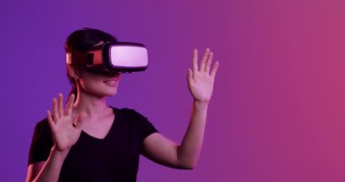 VR kulaklık kullanan Asyalı kadın, mor arka planda dokunmatik ekran, kopyalama alanı, yavaş çekim. Teknoloji, sanal gerçeklik ve metaevren kavramı.