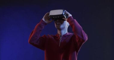 Asyalı adam mavi arka planda video kulaklık kullanıyor, ağır çekimde. Teknoloji, sanal gerçeklik ve metaevren kavramı.