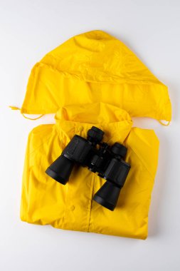 Sarı yağmurluk ve beyaz arkaplanda fotokopi alanı olan dürbünleri kapatın. Ulusal kamp ayı, ekipman ve kutlama konsepti.