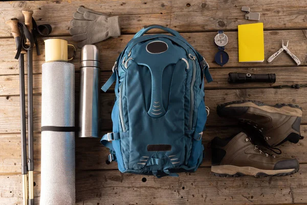 Camping equipment of backpack, mat, thermos and trekking sticks on wooden background. National camping month, equipment and celebration concept.