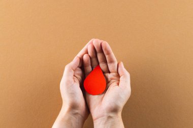Kahverengi arka planda kan damlalarını yudumlayan beyaz bir kadının elleri. Kan bağışı, ilaç ve sağlık hizmetleri.