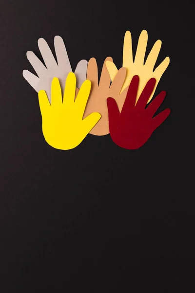 Close up of paper cut out of multi coloured hands with copy space on black background. Humanitarian, people, help and human concept.