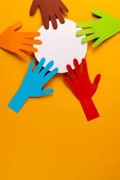 Paper cut out of multi coloured hands and white circle with copy space on orange background. Humanitarian, people, help and human concept.