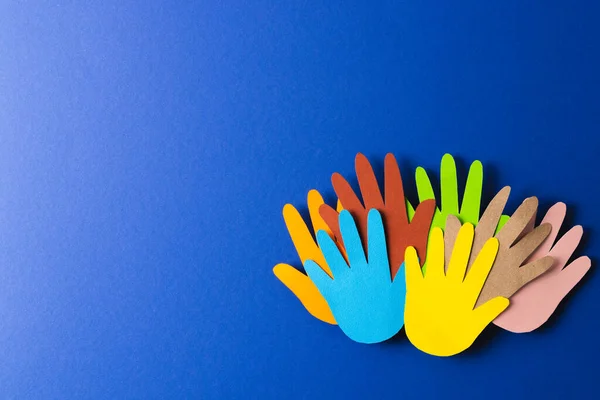 Close up of paper cut out of multi coloured hands with copy space on blue background. Humanitarian, people, help and human concept.