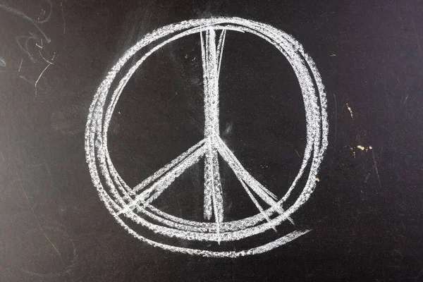 Close up of white chalk peace sign on black chalkboard background. Peace and anti war movement concept.