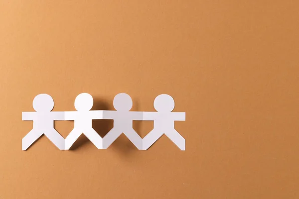 Close up of four paper cut out people figures holding hands with copy space on brown background. Humanitarian, people, help and human concept.