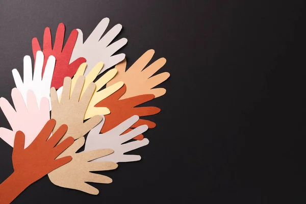 Paper cut out of multi coloured hands with copy space on black background. Humanitarian aid, people, help and human concept.