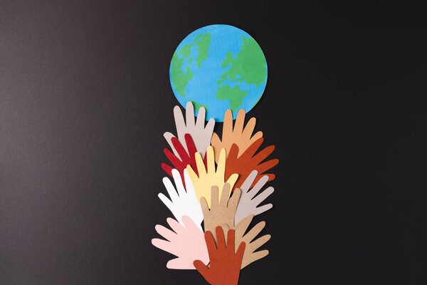 Бумага вырезана из разноцветных рук и глобуса с копировальным пространством на черном фоне. Гуманитарная помощь, люди, помощь и человеческая концепция.